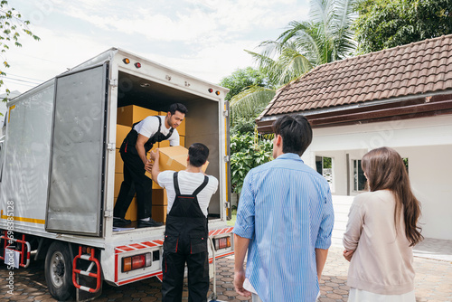 Professional moving service aids a couple in moving to their new house. Teamwork is evident as employees work together unloading and lifting cardboard boxes. Moving Day Concept © sorapop