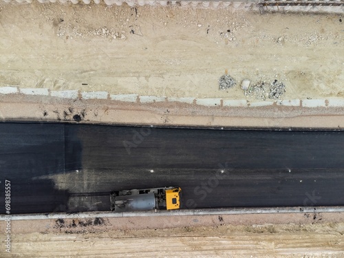 yellow truck pouring bitumen over a new road. Aerial drone shot. Road construction in progress on slope nature canyon. Infrastructure development and logistics.