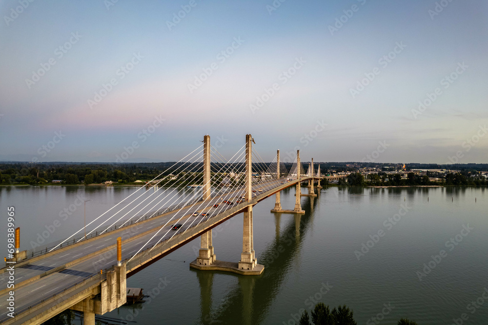 Obraz premium Vancouver, British Columbia, Canada. Aerial view of Fraser River and Golden Ears Bridge during a vibrant winter sunset with heavy road traffic.