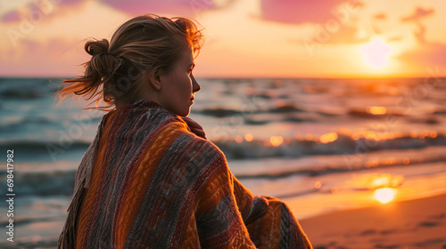 Woman looking at winter sunset on the beach with a shawl on her shoulders on a cold evening