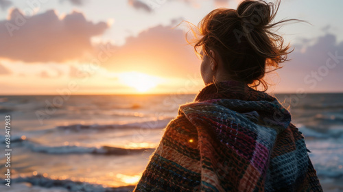 Woman looking at winter sunset on the beach with a shawl on her shoulders on a cold evening photo