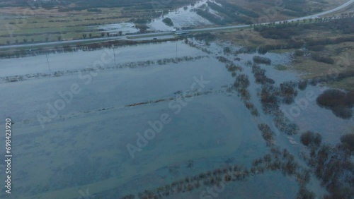 Aerial establishing view of high water, Durbe river (Latvia) flood, brown and muddy water, agricultural fields under the water, overcast winter day with light snow, drone shot moving forward tilt down photo