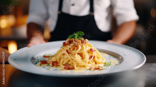Close-up of the chef's hands holding and giving away the finished dish of spaghetti carbonara with bacon, tomatoes and cheese.