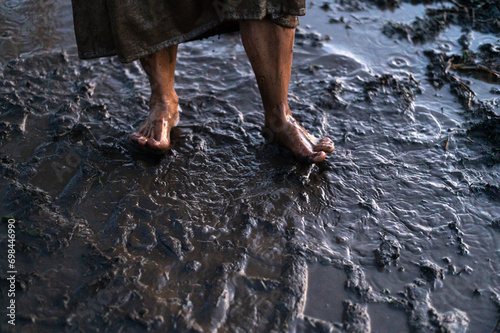 Dirty bare feet of a desperate woman wading through mud puddles photo