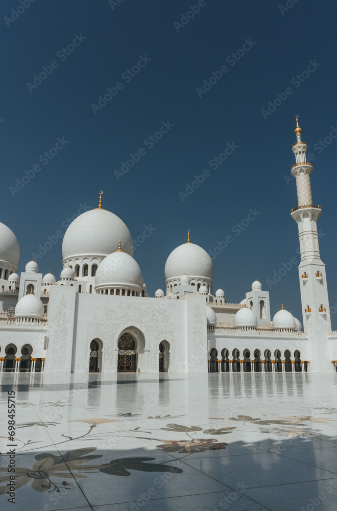 view of Sheikh Zayed Grand Mosque huge tall minarets in white marble muslim symbol and several domes over clear blue sky in uae