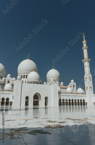 view of Sheikh Zayed Grand Mosque huge tall minarets in white marble muslim symbol and several domes over clear blue sky in uae