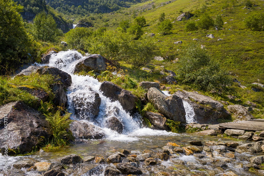 A waterfall in a forest in the green countryside , Europe, France, Occitanie, Hautes-Pyrenees, in summer on a sunny day. A waterfall in a forest in the green countryside , Europe, France, Occitanie, Hautes-Pyrenees, in summer on a sunny day.