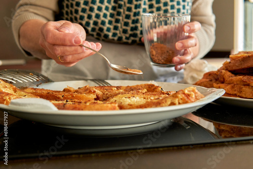 Mujer mayor irreconocible espolvoreando azúcar panela sobre el pan para la receta de torrijas