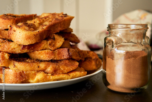 Una pila de torrijas caseras, típicas tostadas francesas españolas para la Cuaresma y Semana Santa, cerca de un frasco de vidrio con canela en polvo. photo