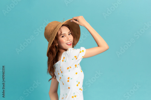 Cheerful young asian woman in summer dress and straw hat isolated on blue background. photo