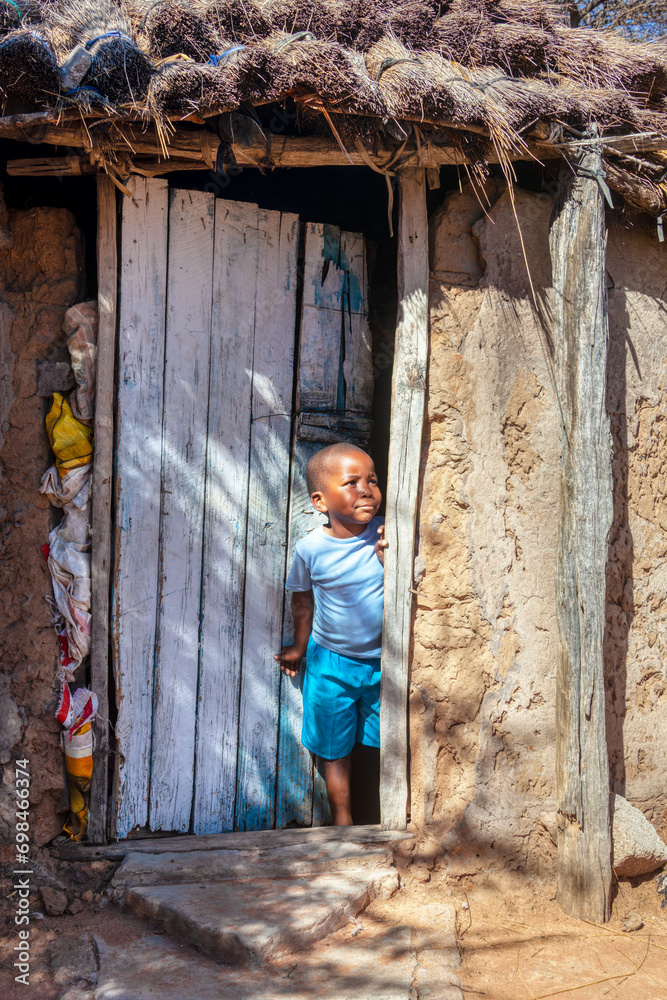 african kid in front of a hut with a thatched roof in the slum