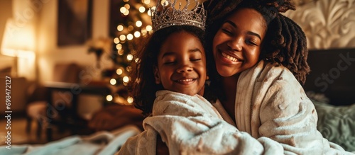 Family bonding at home after a spa day, mother and daughter in bathrobes and crowns, hugging on the couch, smiling. photo