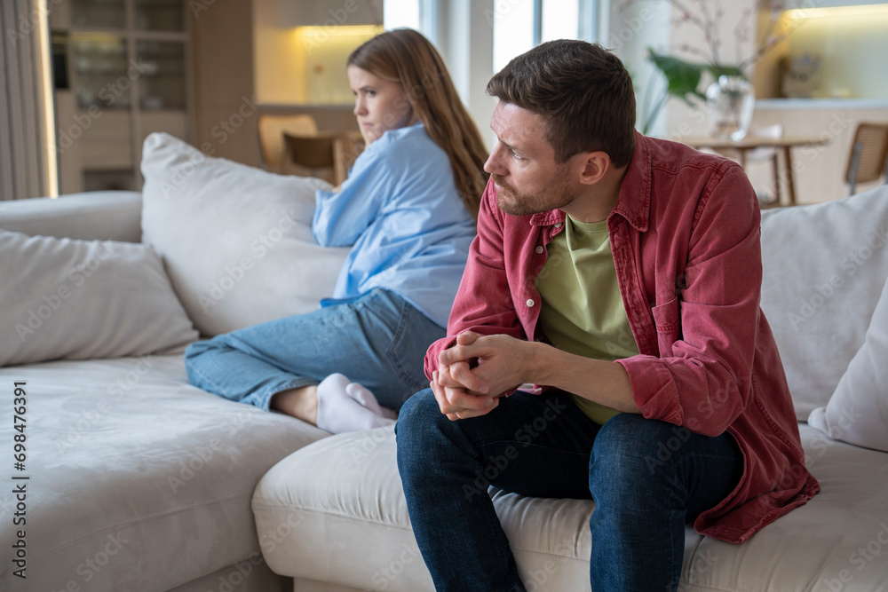 Couple man woman ignoring each other sitting on couch in silence at home turning away. Frustrated spouses offend after family quarrel. Domestic violence abuse neurotic relationships, misunderstanding. - obrazy, fototapety, plakaty 