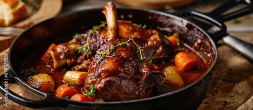 Contemporary slow-cooked lamb shank in red wine sauce with shallots and carrots, served in a stylish stewpot. photo