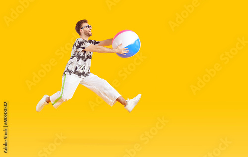 Funny young man tourist wearing casual clothes with inflatable beach ball going on summer holiday trip isolated on studio yellow background and jumping. Vacation  journey and travel concept.