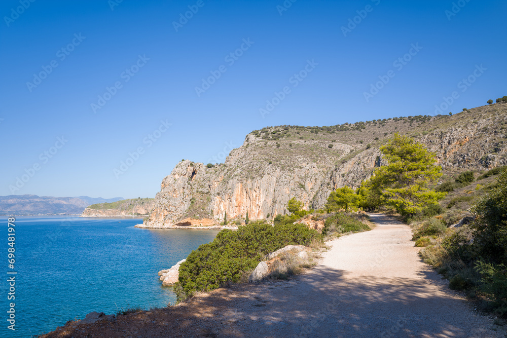 A dirt road on the rocky and arid but green coast, in Europe, Greece, Peloponnese, Argolis, Nafplion, Myrto seashore, in summer, on a sunny day.