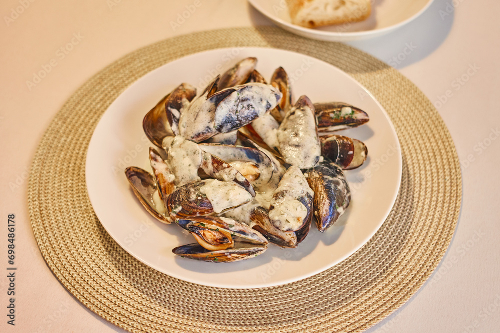 A plate of mussels in cream sauce is served on the table. Cooking mussels in a pan at home.