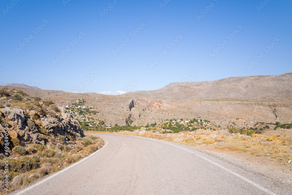 An asphalt road in the middle of arid and rocky mountains , in Europe, Greece, Crete, Kato Zakros, By the Mediterranean Sea, in summer, on a sunny day.