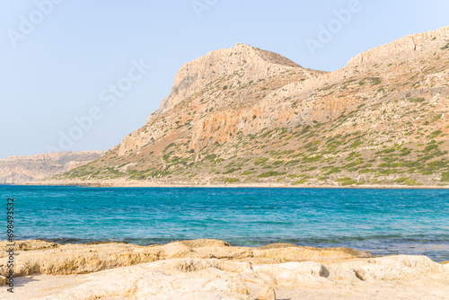 The sandy beach with pink reflections at the foot of the rocky cliffs, in Europe, Greece, Crete, Balos, By the Mediterranean Sea, in summer, on a sunny day.