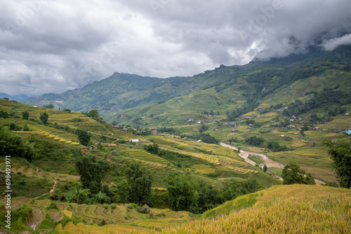 The yellow and green rice terraces above the valley in the green mountains, Asia, Vietnam, Tonkin, Sapa, towards Lao Cai, in summer, on a cloudy day. photo