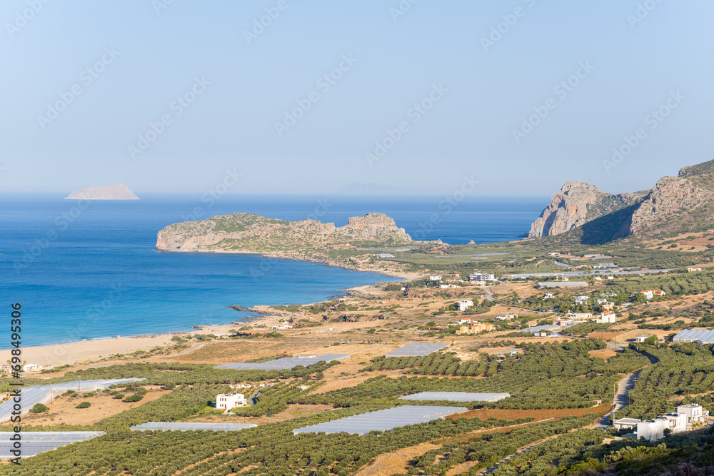 The beach by the greenhouses and olive trees in the countryside , in Europe, in Greece, in Crete, towards Kissamos, towards Chania, By the Mediterranean Sea, in summer, on a sunny day.
