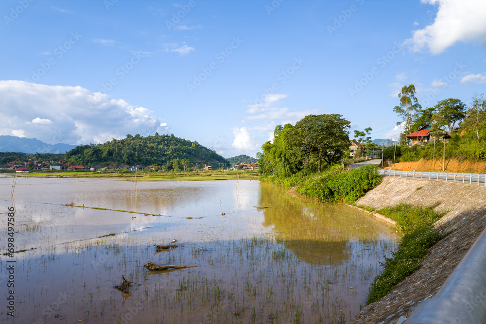 A lake and the flooded rice fields in the green countryside near the mountains, Asia, Vietnam, Tonkin, Dien Bien Phu, in summer, on a sunny day. A lake and the flooded rice fields in the green countryside near the mountains, Asia, Vietnam, Tonkin, Dien Bien Phu, in summer, on a sunny day.
