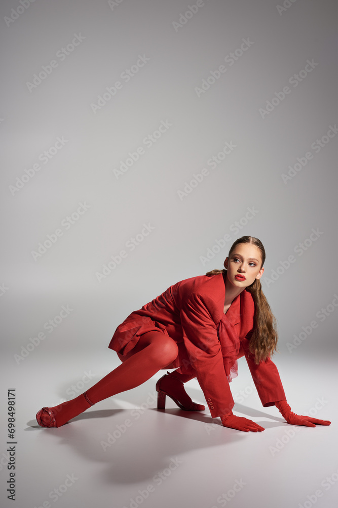 high fashion young model in red stylish outfit looking away while posing on grey background