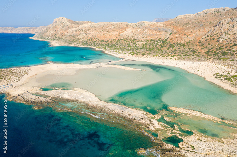 The sandy beach with pink reflections at the foot of the rocky cliffs, in Europe, Greece, Crete, Balos, By the Mediterranean Sea, in summer, on a sunny day. The sandy beach with pink reflections at the foot of the rocky cliffs, in Europe, Greece, Crete, Balos, By the Mediterranean Sea, in summer, on a sunny day.