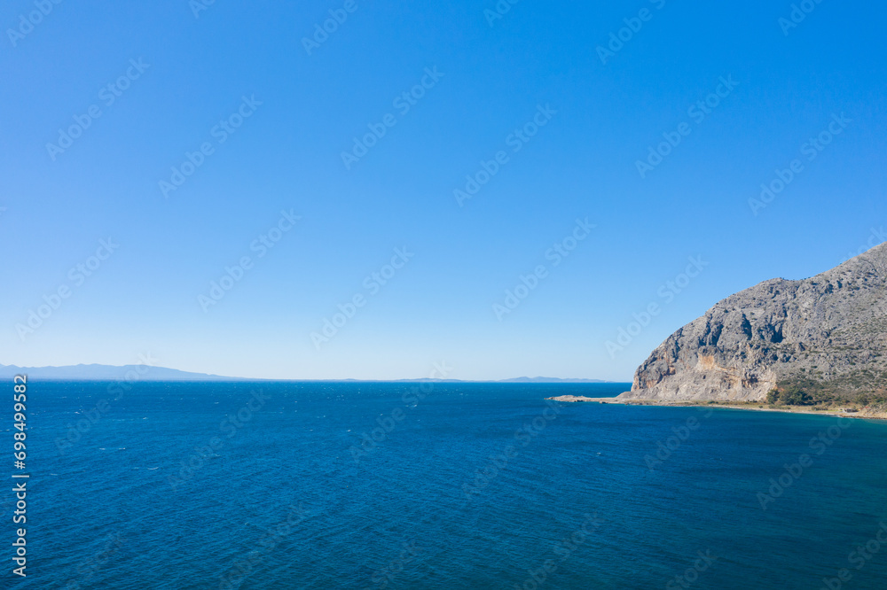 The arid rocky coast and its green countryside, in Europe, in Greece, in Aetolia Acarnania, towards Patras, by the Ionian Sea, in summer, on a sunny day.