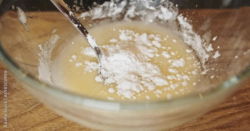White powdered sugar crumbles into a plate. The process of preparing the sweet glaze for the dessert.