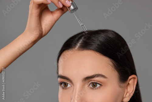 Beautiful woman applying hair serum on grey background, closeup. Cosmetic product