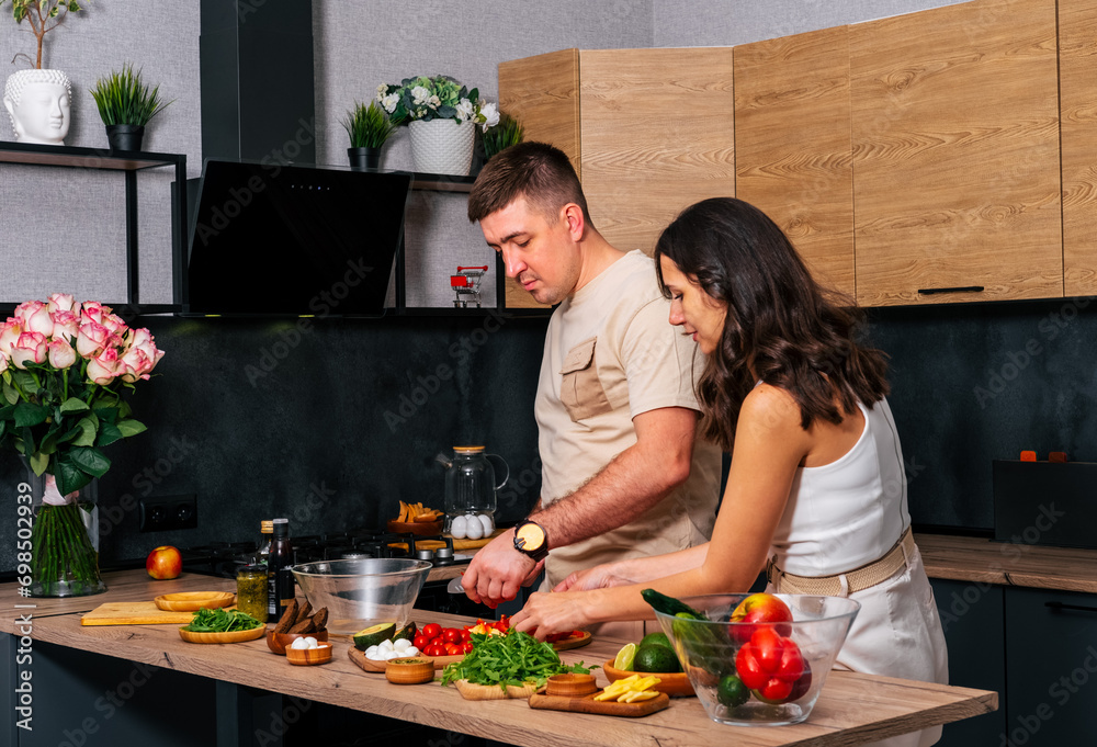 Young man cooking salad at the kitchen and his happy wife hugging him. Young man cooking salad at the kitchen and his happy wife hugging him.