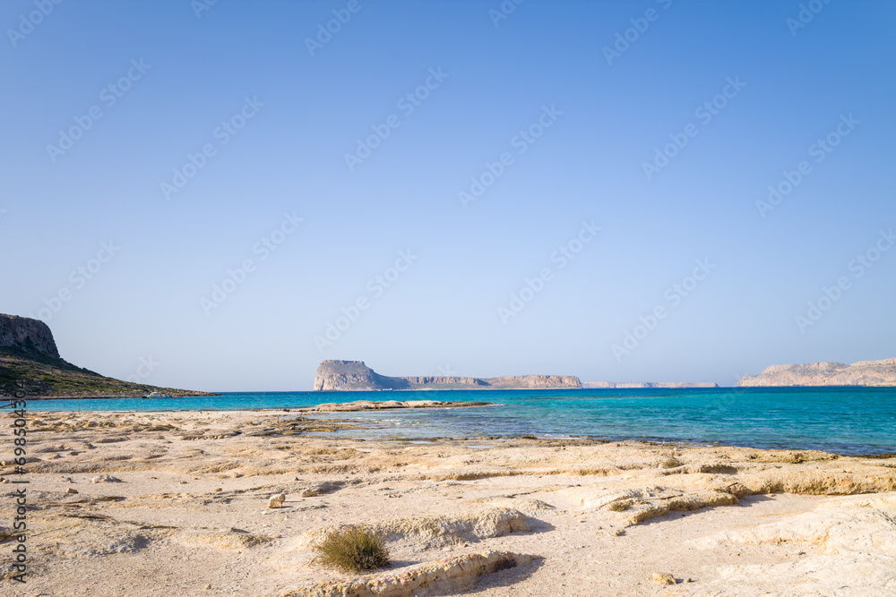 The sandy beach with pink reflections at the foot of the rocky cliffs, in Europe, Greece, Crete, Balos, By the Mediterranean Sea, in summer, on a sunny day. The sandy beach with pink reflections at the foot of the rocky cliffs, in Europe, Greece, Crete, Balos, By the Mediterranean Sea, in summer, on a sunny day.