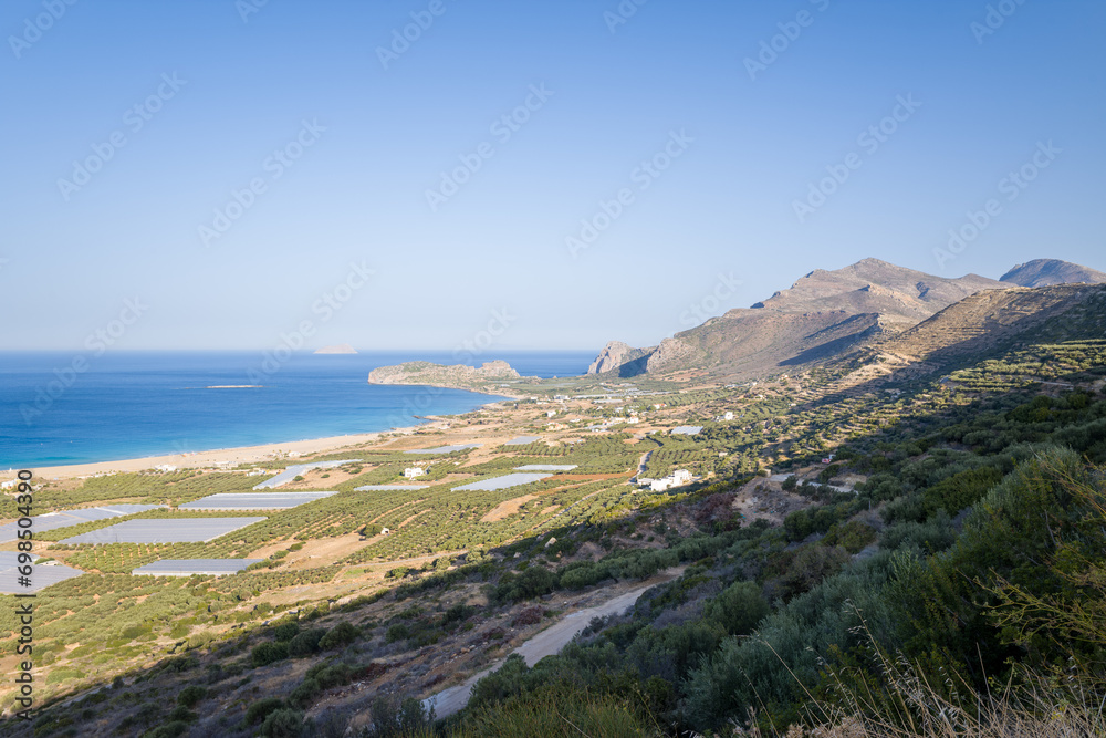 The beach by the greenhouses and olive trees in the countryside , in Europe, in Greece, in Crete, towards Kissamos, towards Chania, By the Mediterranean Sea, in summer, on a sunny day.