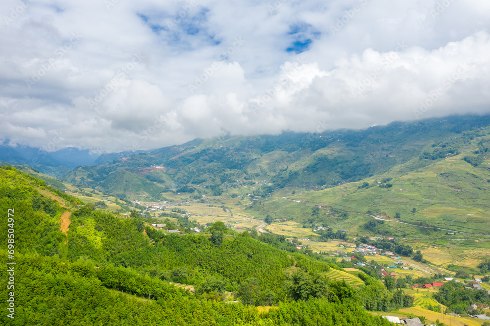 The traditional village on the mountainsides with tropical forests with green and yellow rice terraces, in Asia, Vietnam, Tonkin, Sapa, towards Lao Cai, in summer, on a cloudy day.