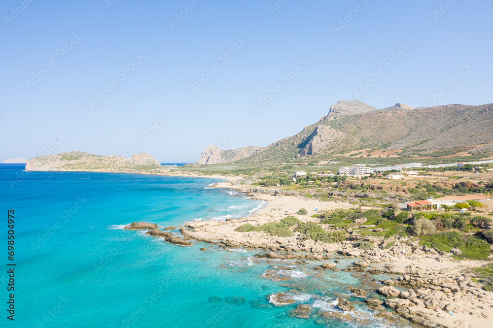 The sandy beach at the foot of the rocky cliffs in the arid countryside , in Europe, Greece, Crete, towards Kissamos, towards Chania, By the Mediterranean Sea, in summer, on a sunny day.
