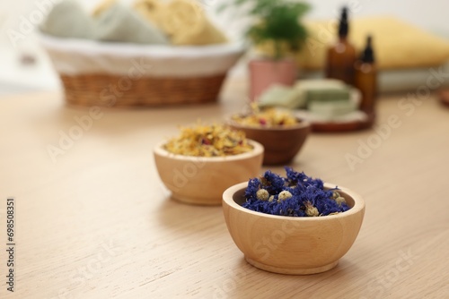 Bowls of dry flowers on light wooden table, space for text. Spa therapy