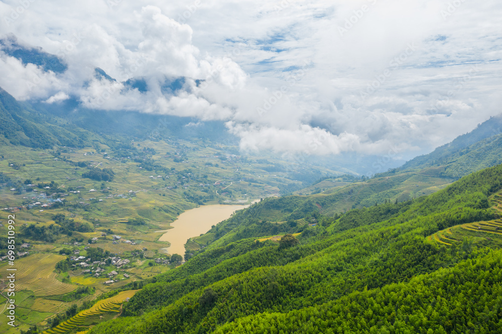 The green and yellow rice fields in the mountains in the verdant valley, Asia, Vietnam, Tonkin, Sapa, towards Lao Cai, in summer, on a cloudy day.
