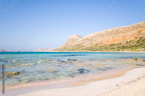 Fototapeta Naklejka Na Ścianę i Meble -  The sandy beach with pink reflections at the foot of the rocky cliffs, in Europe, Greece, Crete, Balos, By the Mediterranean Sea, in summer, on a sunny day.