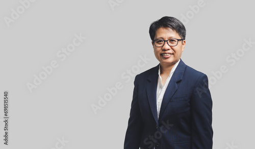 Businesswoman with short black hair in a suit stands looking at the camera with a smile while standing on a gray background.