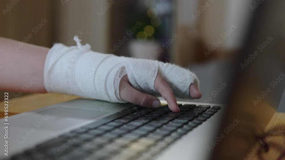 Closeup of pressing keys on keyboard with free fingers on injured hand. Child uses laptop with