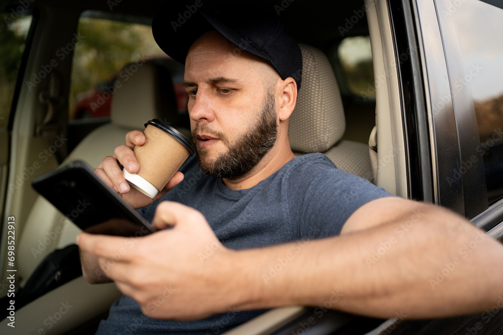 Male bearded driver with a smartphone in hand and paper cup of hot coffee. Concept of inattention at the wheel, rest and coffee break Male bearded driver with a smartphone in hand and paper cup of hot coffee. Concept of inattention at the wheel, rest and coffee break