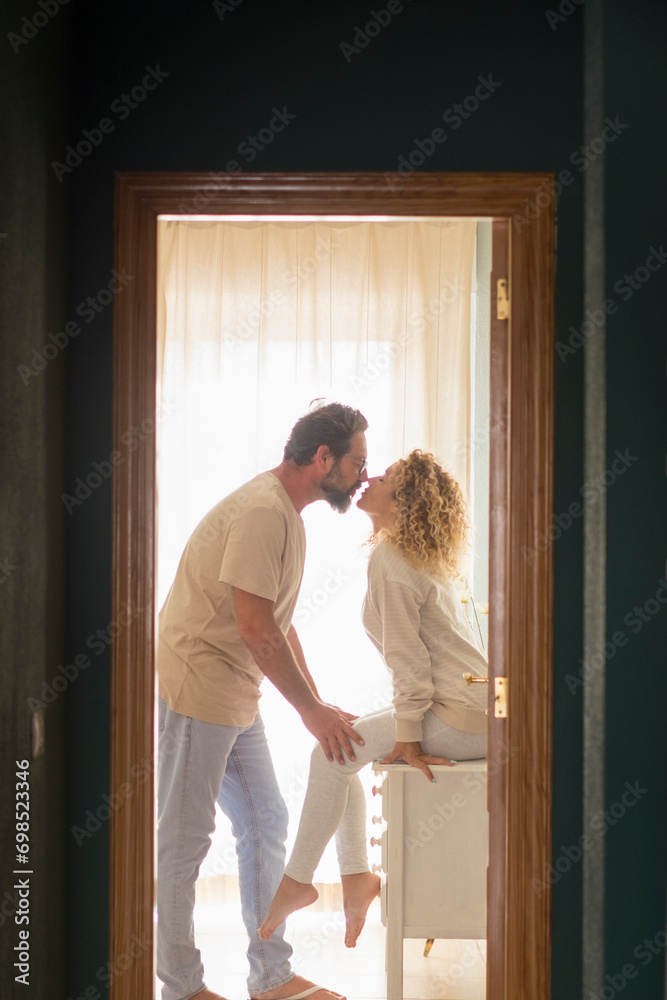 Romantic couple kissing at home - happy relationship man and woman indoor - husband and wife kiss with love and passion with window light in background - concept of happiness and togetherness Romantic couple kissing at home - happy relationship man and woman indoor - husband and wife kiss with love and passion with window light in background - concept of happiness and togetherness