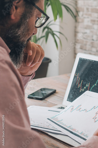 One man looking and studying stock market charts at the desk with opened laptop and connection. Concept of economy crypto forex exchange business job. Modern worker analyses busy in home workplace photo