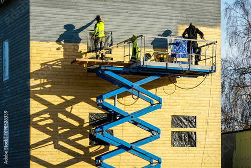 Residential house facade painting works after cladding with wooden planks using scissor lift platform photo