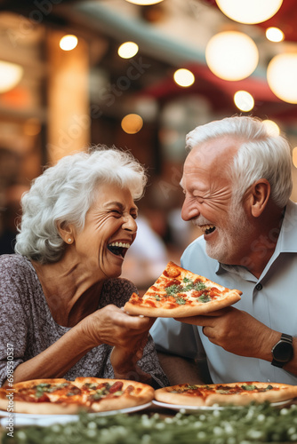 Couple of elderly gentlemen with white hair are smiling while eating a pizza. Celebrating anniversary in pizzeria sitting outdoors. Happy people concept
