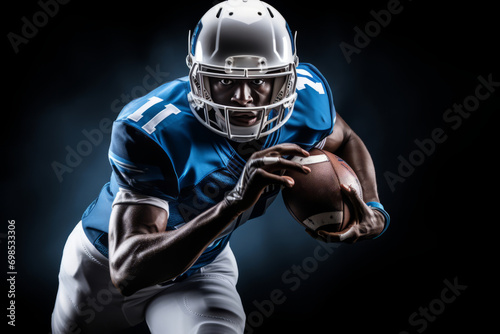 Portrait of American football player running with the ball. Muscular athlete in a blue and white uniform with an ovoid ball in a dynamic pose. Isolated on black background.