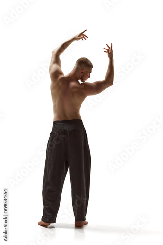 Rear view of shirtless man with naked torso wearing trousers posing raising hands up against white studio background. Concept of men's health, beauty, body and skin care, fitness. Body art © Lustre Art Group 
