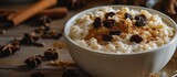 White ceramic bowl with rice pudding topped by raisins and cinnamon on a table.
