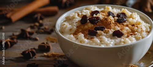 White ceramic bowl with rice pudding topped by raisins and cinnamon on a table.